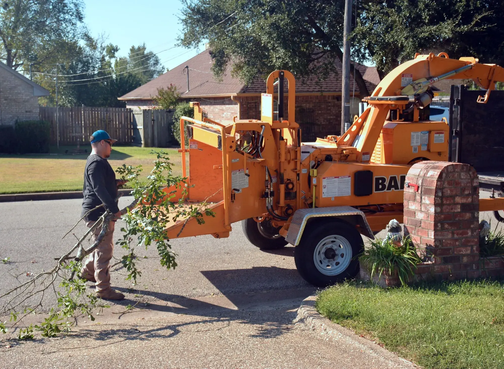 A tree crew feeding cut branches into a wood chipper at the curb in front of a house