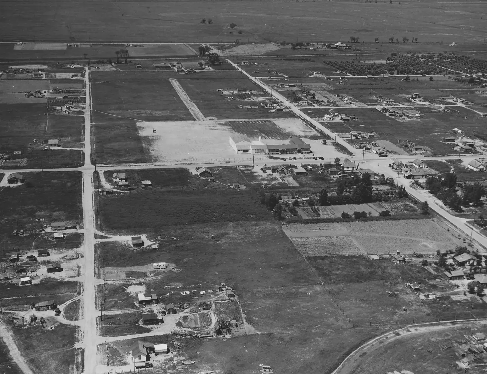 Black-and-white aerial view of Olivehurst in April 1940, with dirt streets, scattered new houses, and orchard rows beyond the fields