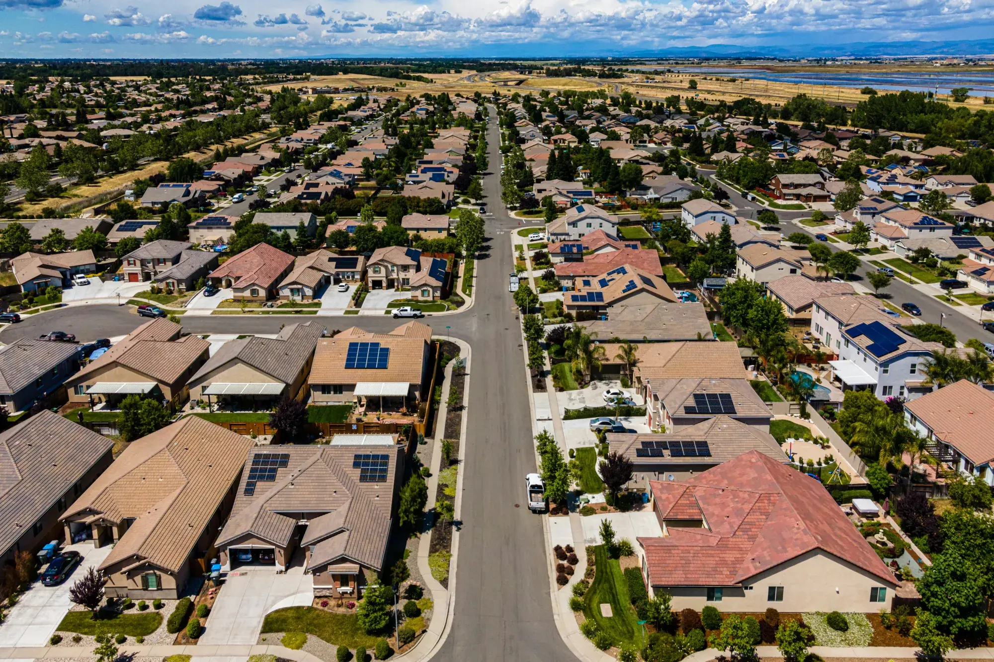 Aerial view of a valley neighborhood: tile-roofed homes along wide streets, with farmland beyond