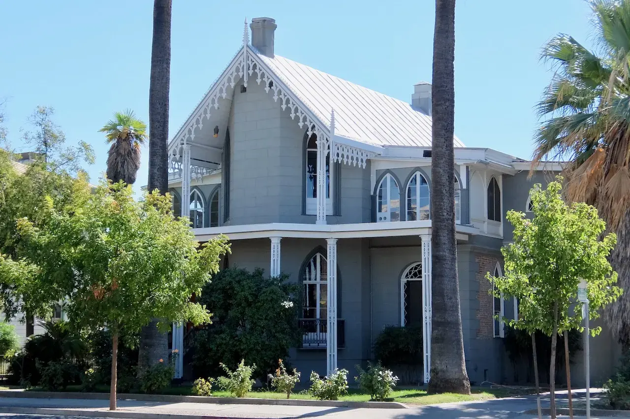 The 1850s Gothic Revival Ramirez House on Fifth Street in Marysville, California, between tall palms and young street trees